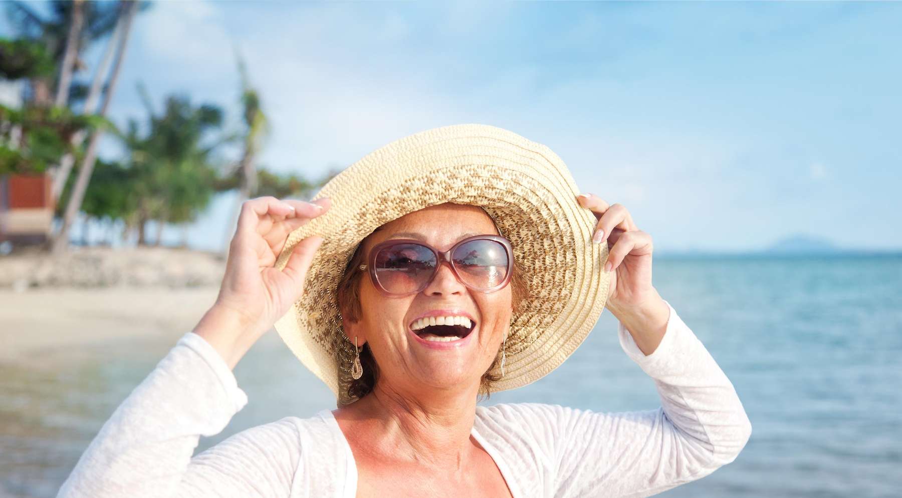 woman with sunglasses and sun hat smiling at the beach