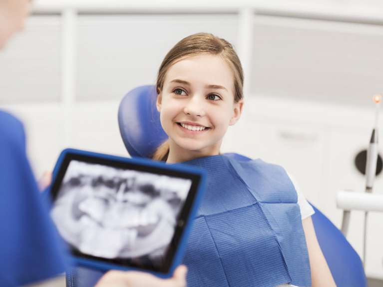 girl sitting in dental chair smiling while dentist holds x-rays